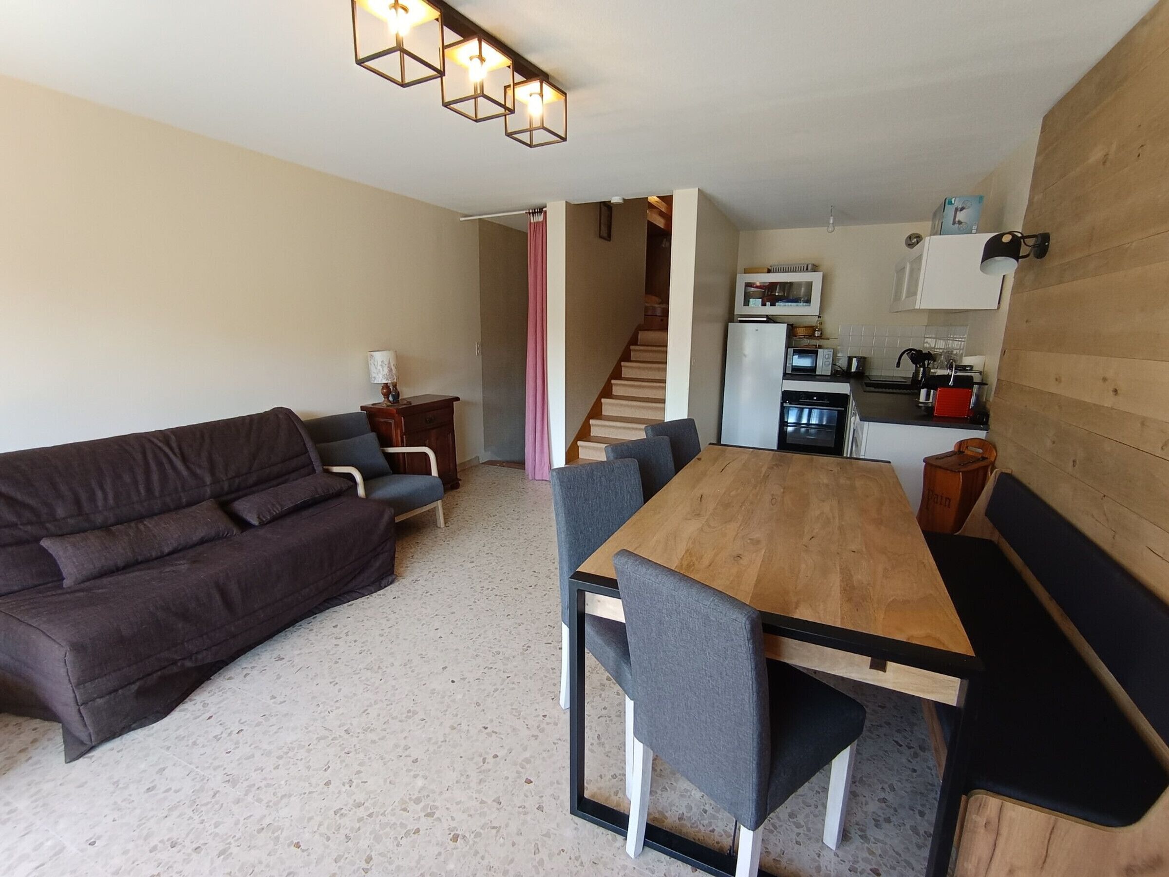En kompakt opholdsstue med sofa, spisebord, stole, et køkken og en trappe.
