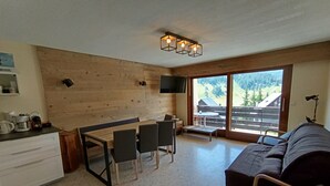 Un salon moderne avec un mur en bois, un coin repas comprenant une table et des chaises, un canapé et une grande fenêtre donnant sur l’extérieur.