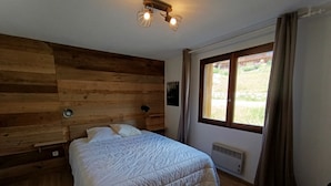 Une chambre à coucher avec une tête de lit en bois, un grand lit avec une literie blanche, une fenêtre avec des rideaux et un luminaire au plafond.