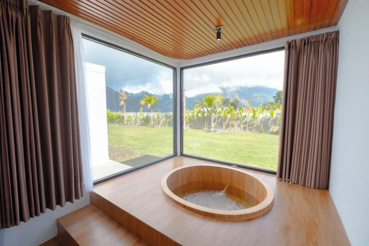 Ein modernes Badezimmer mit einer Holzbadewanne, großen Fenstern und Blick auf einen Garten und Berge.