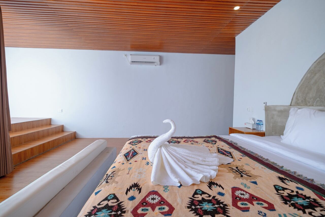 A hotel room with a bed, a patterned rug, a white swan decoration, a wooden staircase, and a wall-mounted air conditioning unit.