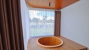 A modern room with a wooden bathtub, large windows with sheer curtains, and a view of a garden. - Lake Batur Villa (Kintamani)