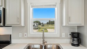 Eine Küche mit doppelter Spüle, einem Fenster mit Blick auf ein Feld und einen Wohnwagen, sowie eine Kaffeemaschine auf der Arbeitsplatte.