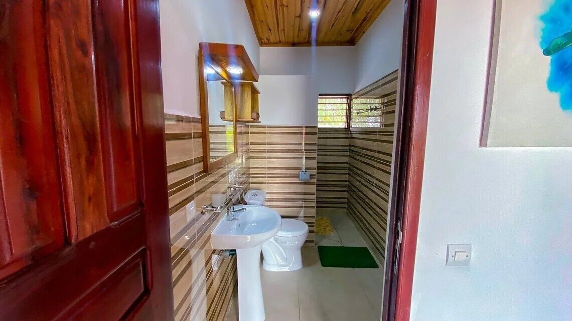 Un baño con techo de madera, paredes a rayas, un lavamanos y un inodoro.