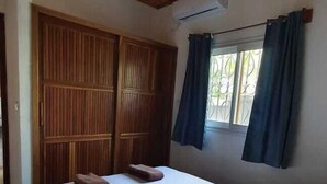 A bedroom with a wooden ceiling, a large bed, a wardrobe, and a window with curtains. - Jardin fleuri de Lety (Nosy Be)