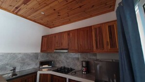 A kitchen with wooden cabinets, a gas stove, a coffee maker, and a stainless steel refrigerator. - Jardin fleuri de Lety (Nosy Be)