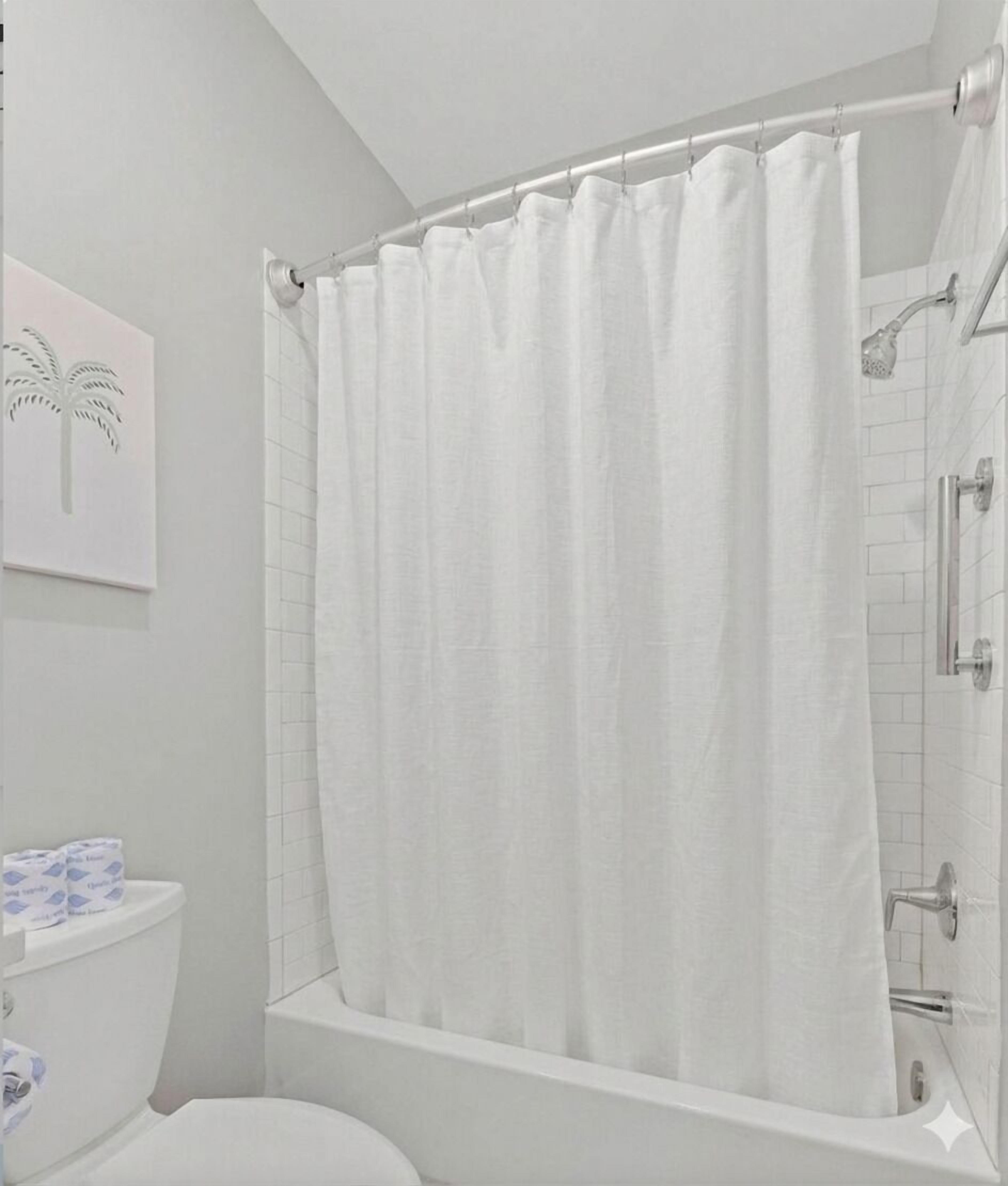 Een badkamer met een witte douchegordijn, een toilet en een toiletrolhouder.
