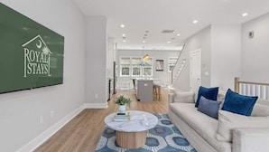 A modern living room with a sofa, coffee table, and a TV mounted on the wall displaying "ROYAL STAYS". - Sincerely Shem III- 7 min to beach and dtwn CHS (Mount Pleasant)