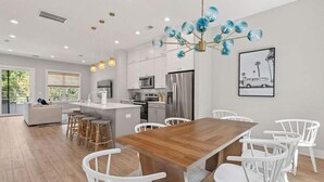 A modern kitchen with white cabinets, stainless steel appliances, and a wooden dining table surrounded by white chairs. - Sincerely Shem III- 7 min to beach and dtwn CHS (Mount Pleasant)