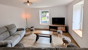 A modern living room with a grey sofa, a wooden coffee table, and a TV on a wooden stand. - Charming cottage in Southern Vosges, perfect for 14 guests (Les Fessey)