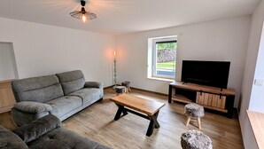 A modern living room with a grey sofa, wooden coffee table, and a TV on a wooden stand. - Charming cottage in Southern Vosges, perfect for 14 guests (Les Fessey)