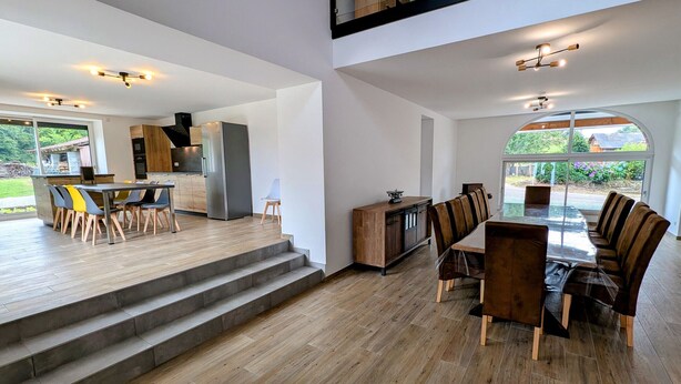 A spacious dining area with a large table and chairs, a kitchen area with modern appliances, and a view of the outdoors through large windows. - Charming cottage in Southern Vosges, perfect for 14 guests (Les Fessey)