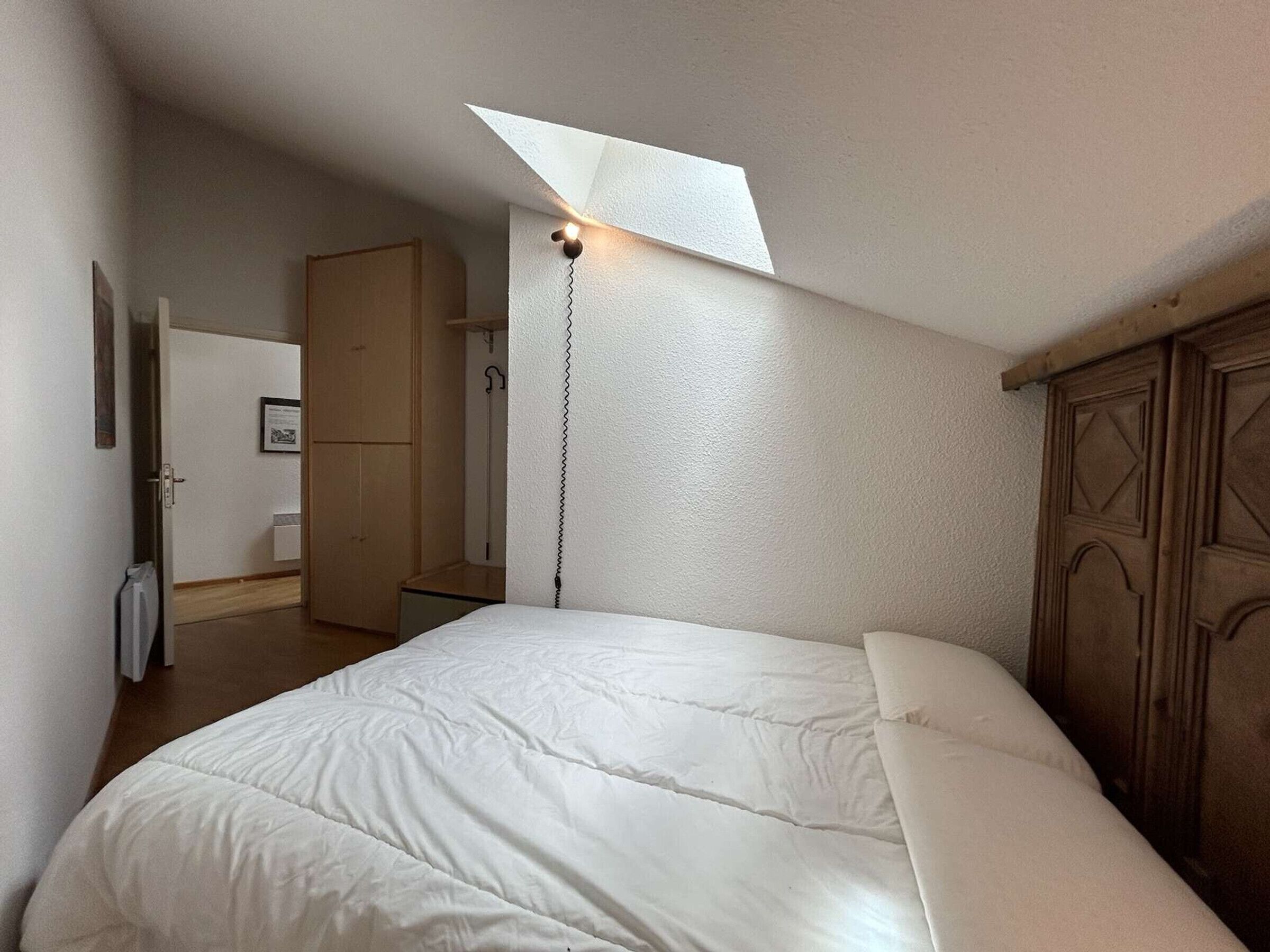 Un dormitorio con una cama grande, un armario de madera y un tragaluz.