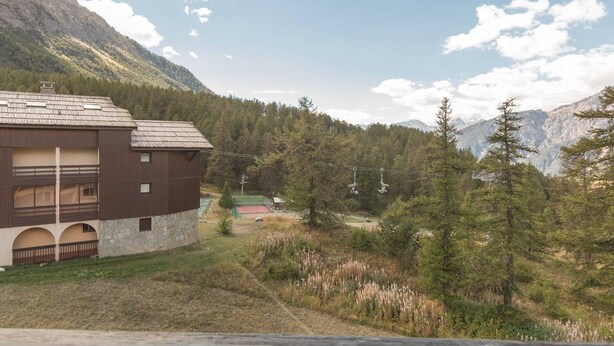A two-story building with a stone foundation and a brown roof, surrounded by a forested area and mountains in the background. - Cozy apartment for 6 in Montgenèvre, pet-friendly with parking (Montgenèvre)