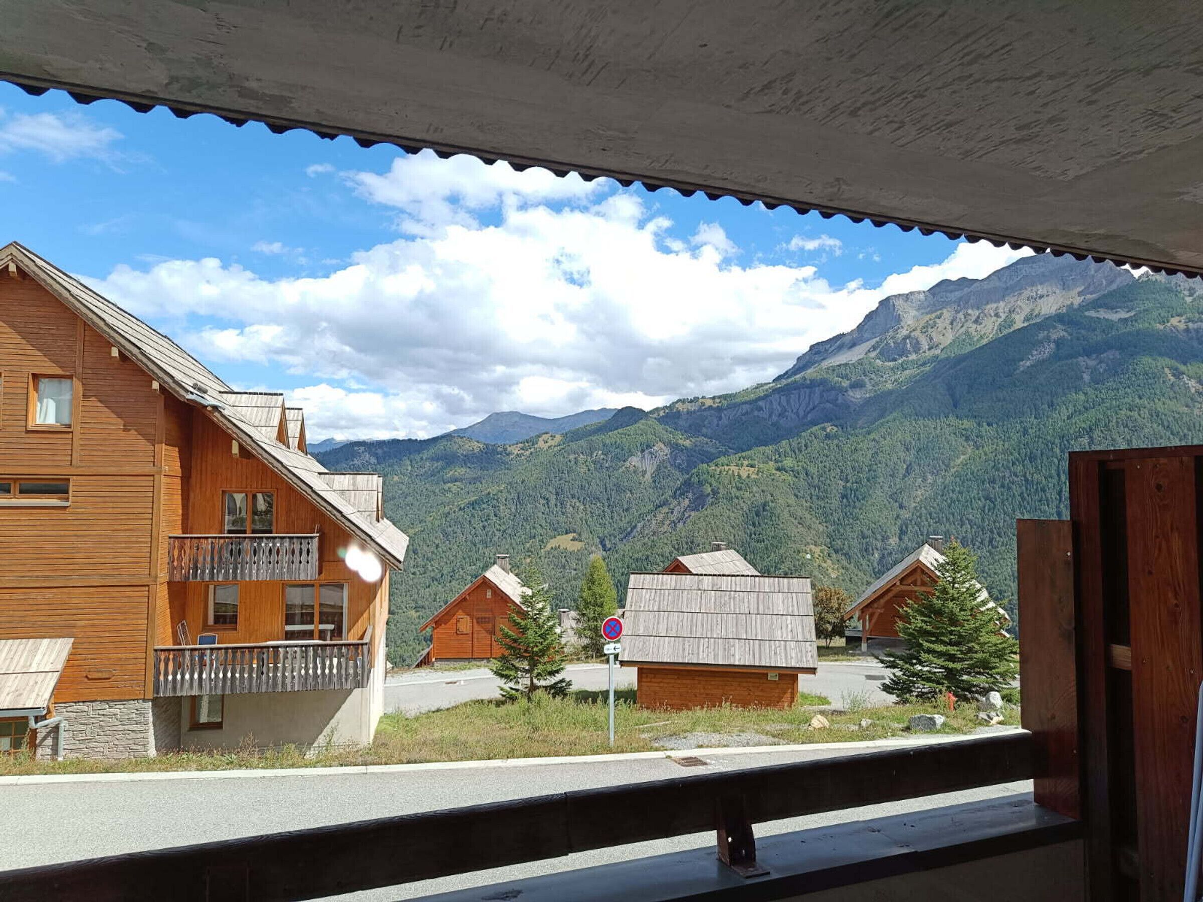 A wooden cabin with a balcony, surrounded by mountains and a clear sky.
