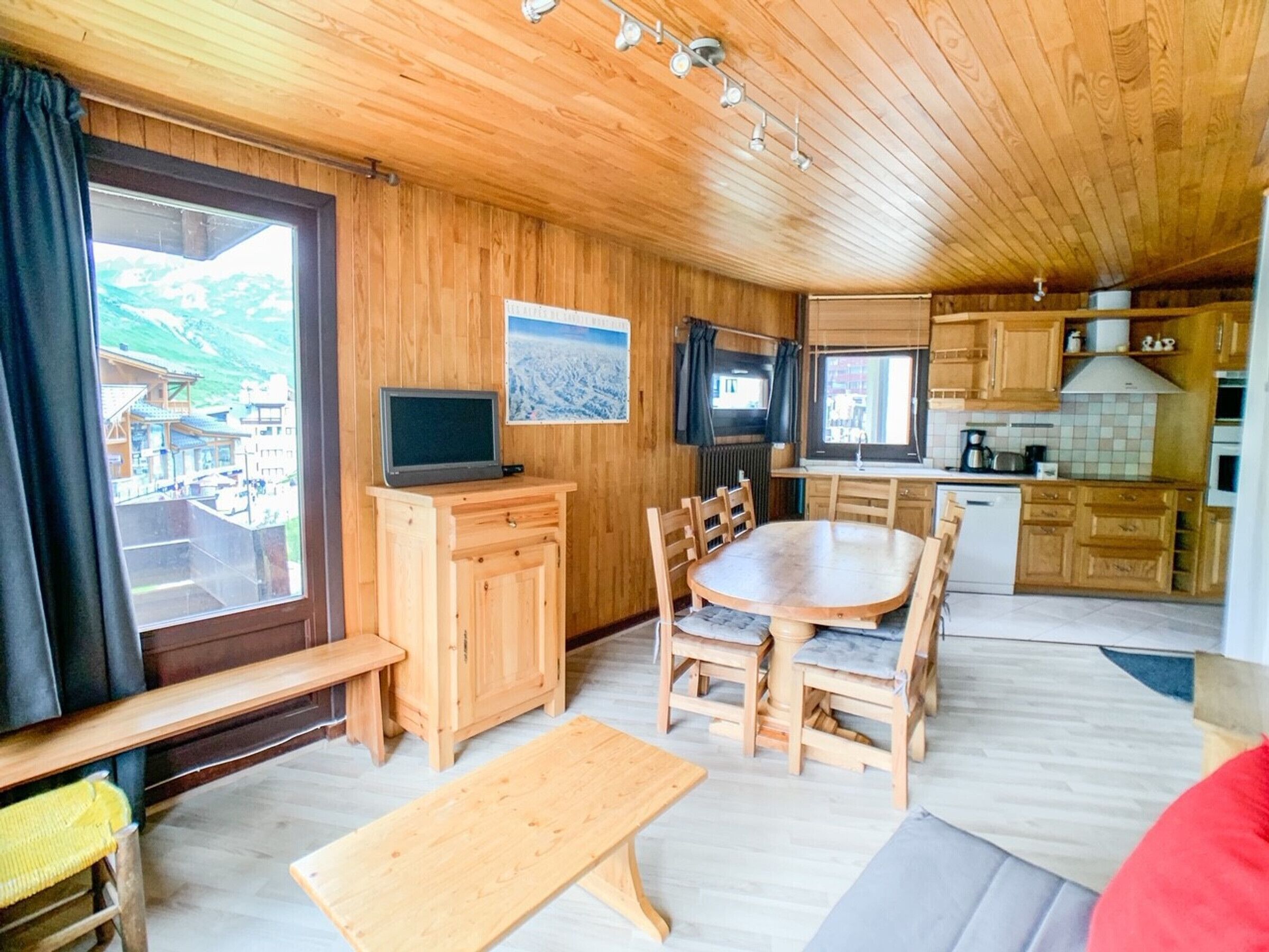 Un intérieur en bois comprenant une table à manger, des chaises, un téléviseur posé sur un meuble et un coin cuisine.