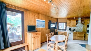 A wooden interior with a dining table, chairs, a TV on a cabinet, and a kitchen area.