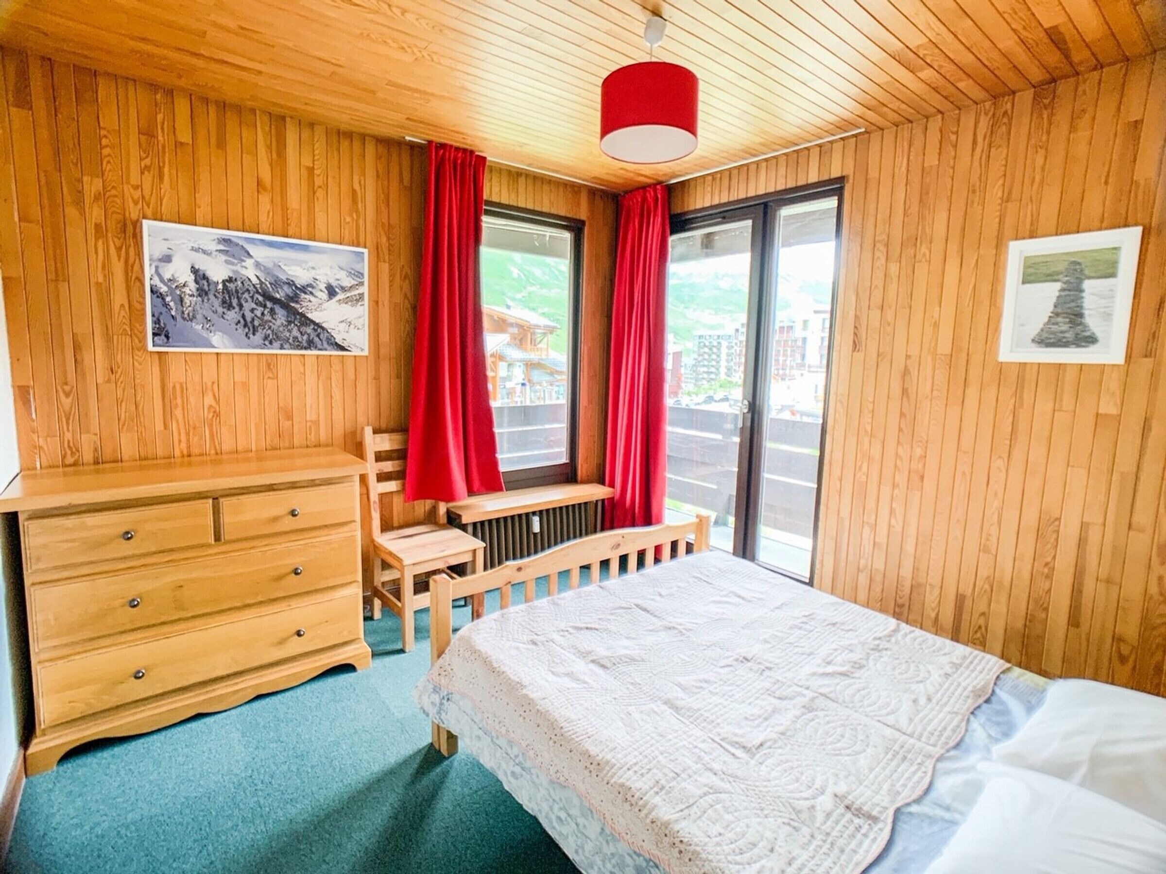 A wooden-paneled room with a bed, a wooden dresser, and a bench by the window.