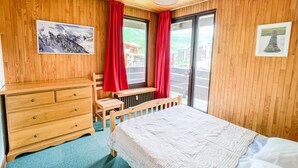 A wooden-paneled room with a bed, a wooden dresser, and a bench by the window.