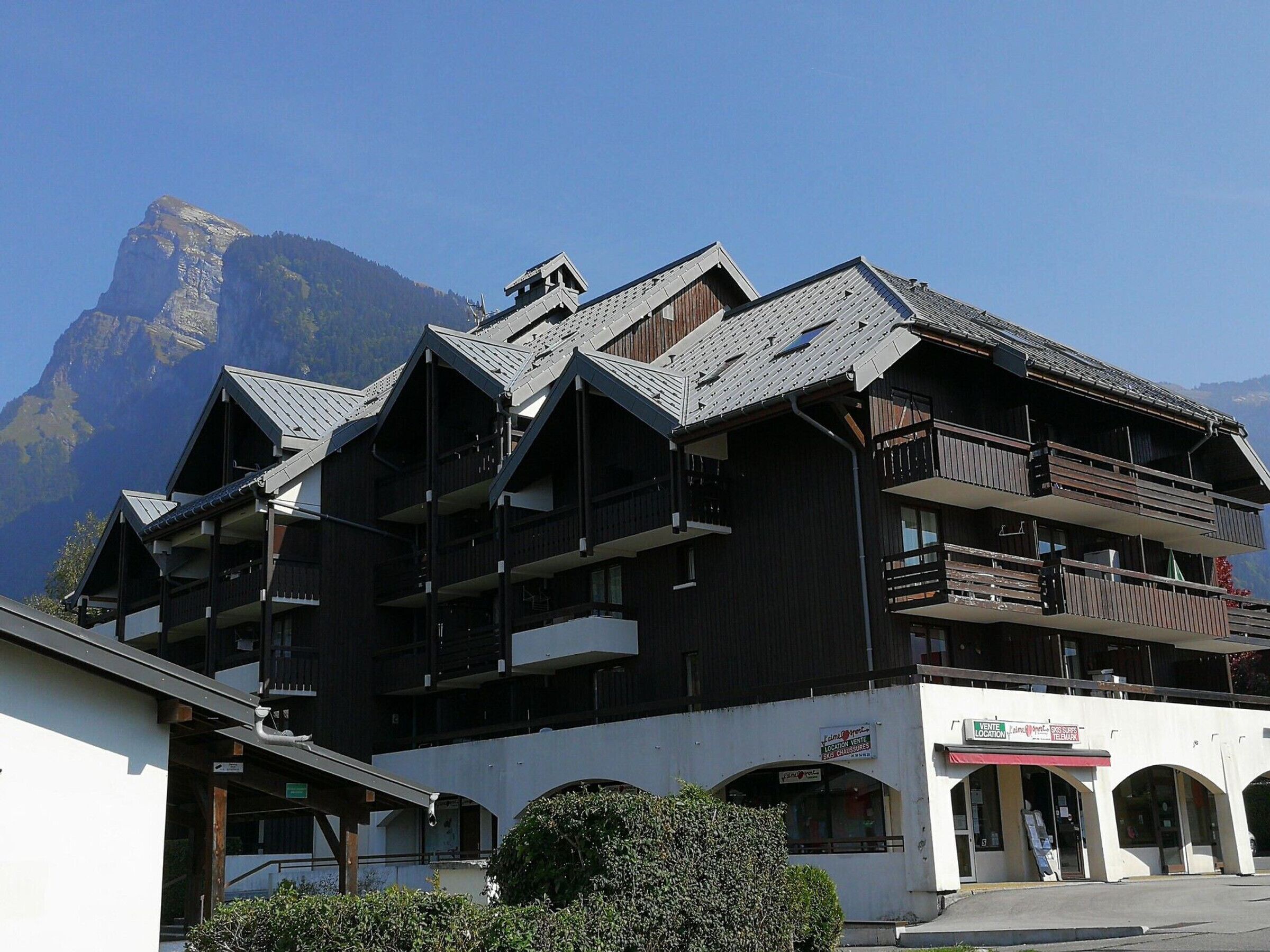 Un edificio a più piani con balconi, un cartello da località sciistica e montagne sullo sfondo.
