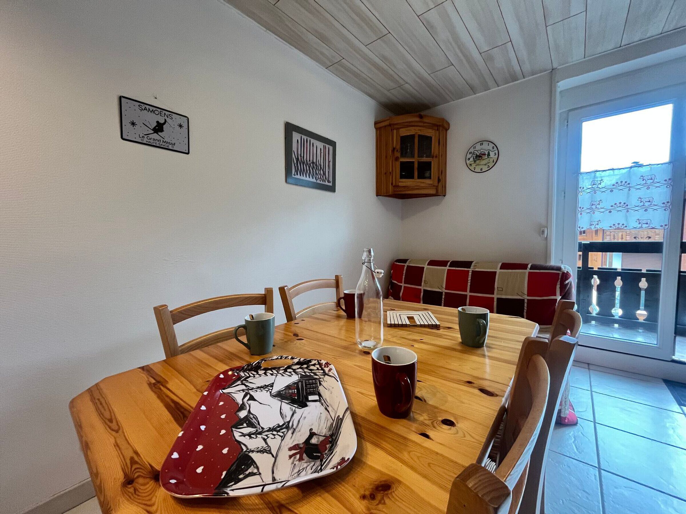 Un espace repas comprenant une table en bois, des chaises, un banc et une vue sur l’extérieur.