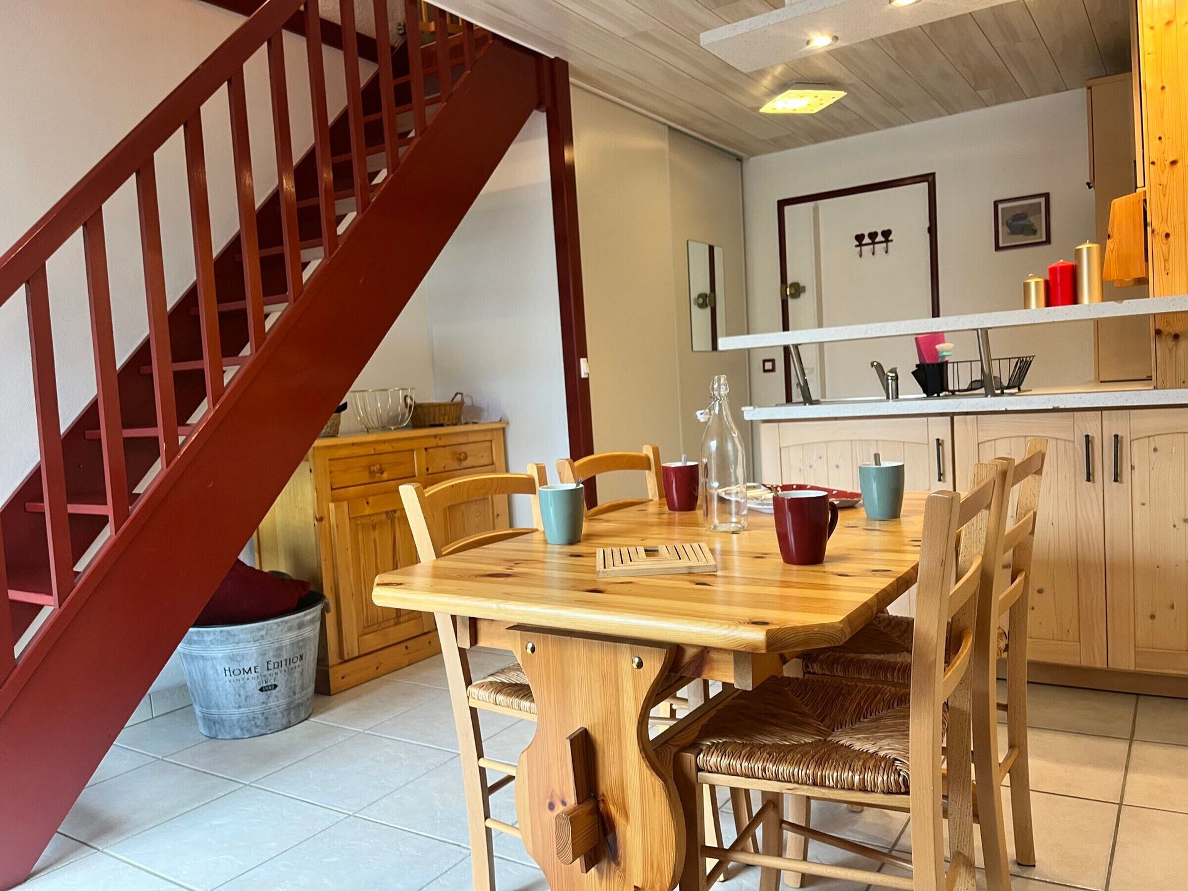 Une table à manger en bois avec des chaises, un coin cuisine avec des meubles en bois et un escalier avec des rampes en bois.