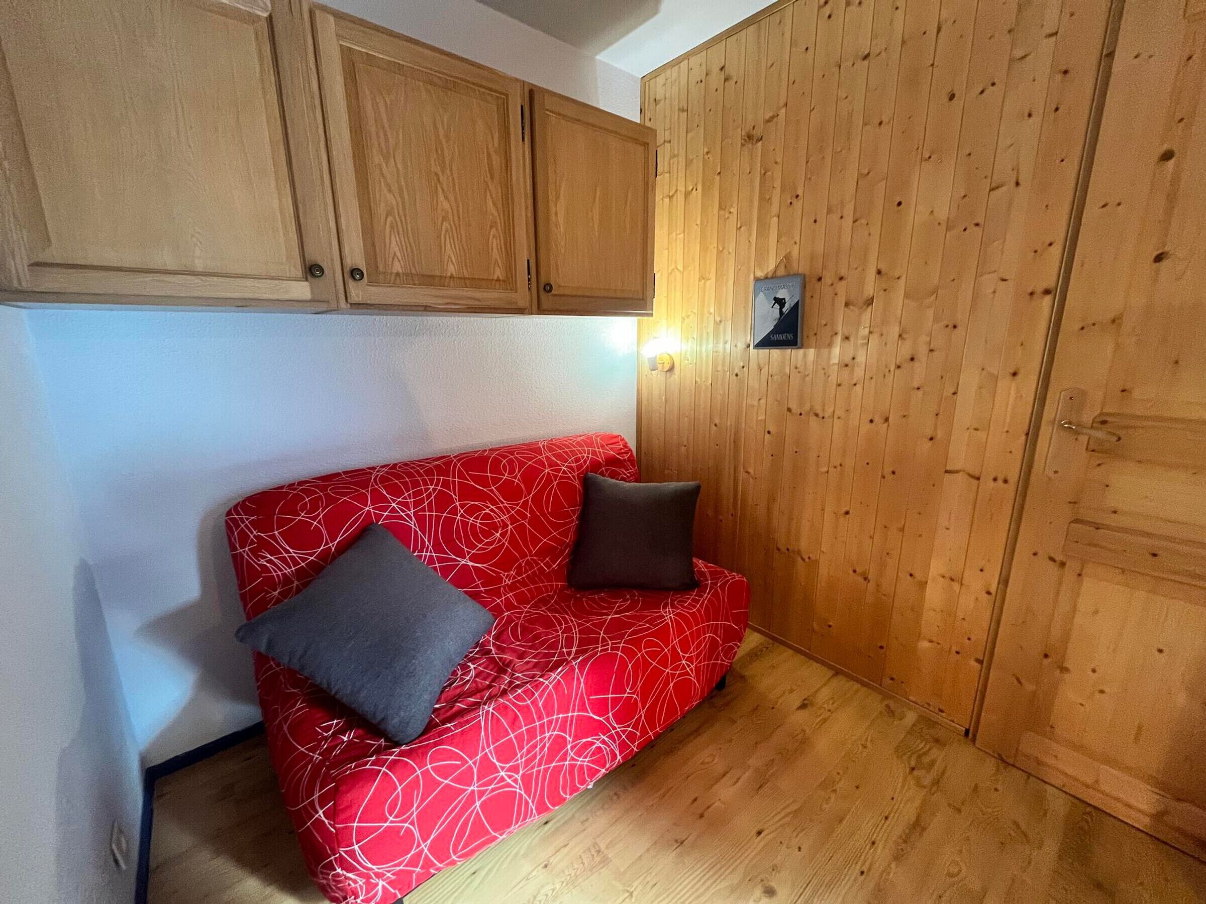 Ein kleiner Raum mit einem roten, gemusterten Sofa, zwei Kissen, Holzschränken und einer Holzpaneele verkleideten Wand.