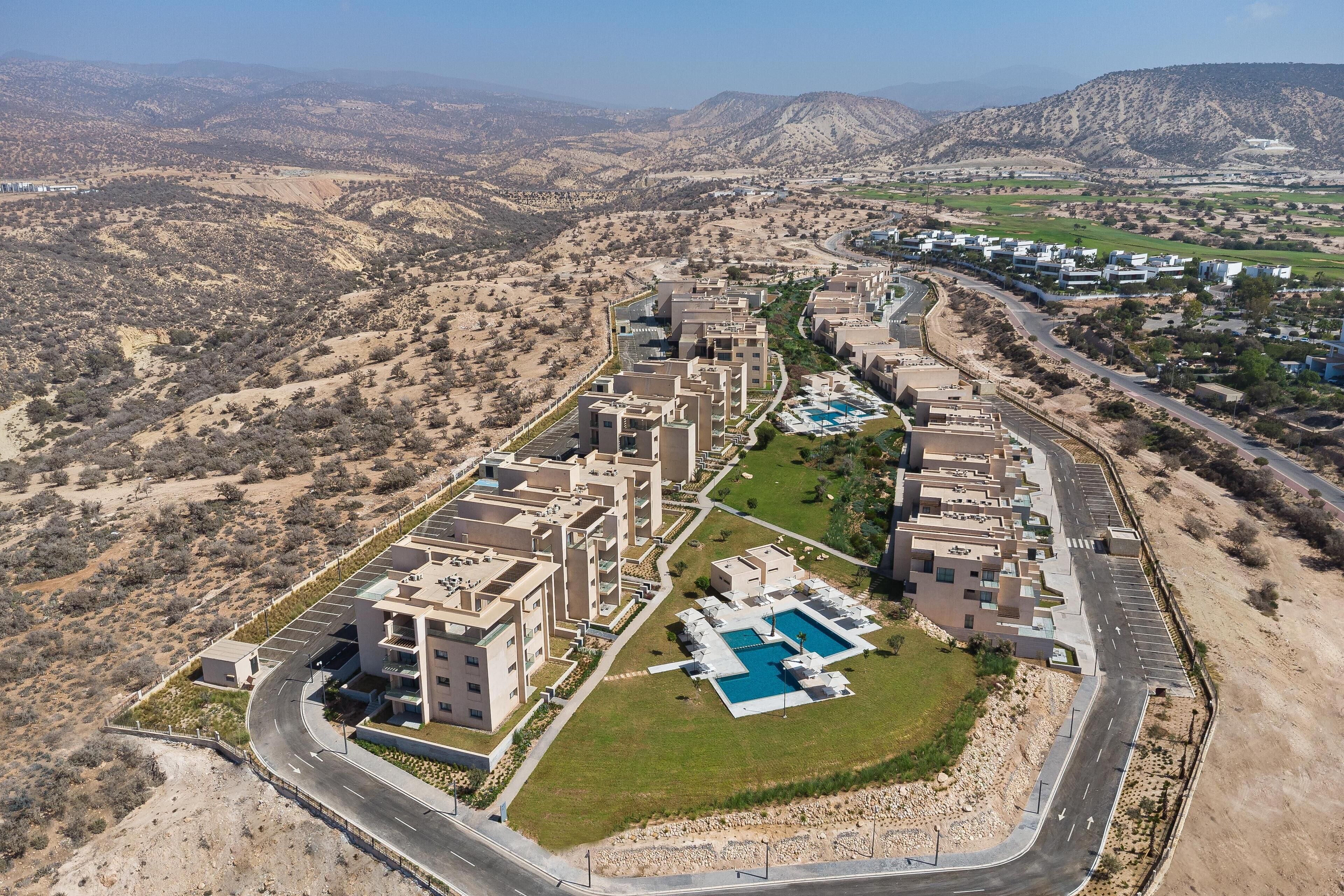 Eine Vogelperspektive eines modernen Resorts mit mehreren Gebäuden, einem Schwimmbecken und einer kurvenreichen Zufahrtsstraße.