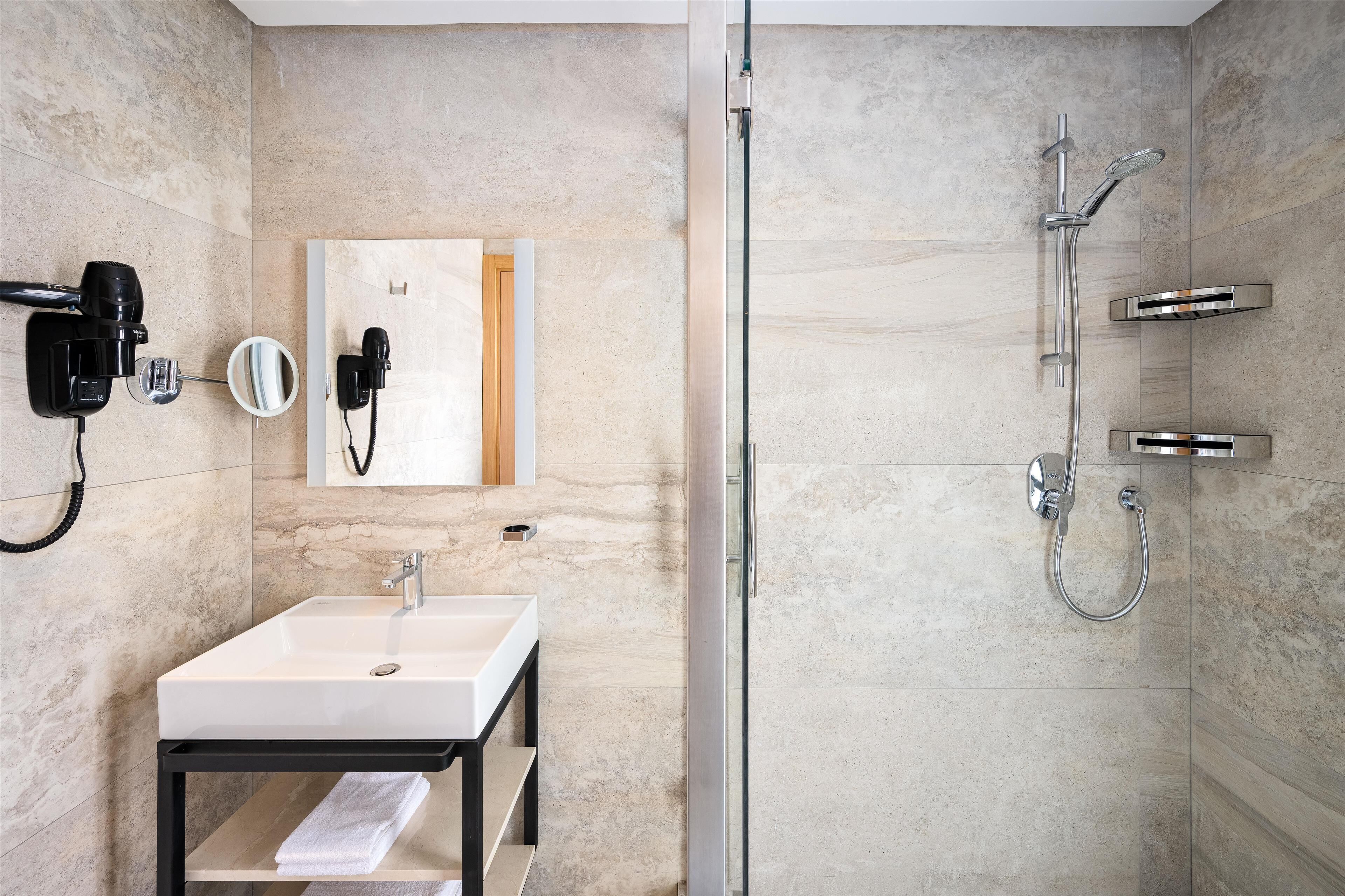 A modern bathroom with a glass-enclosed shower, a white sink, and a mirror with a hairdryer.