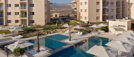 A modern hotel with a central swimming pool, multiple balconies, and outdoor seating areas.