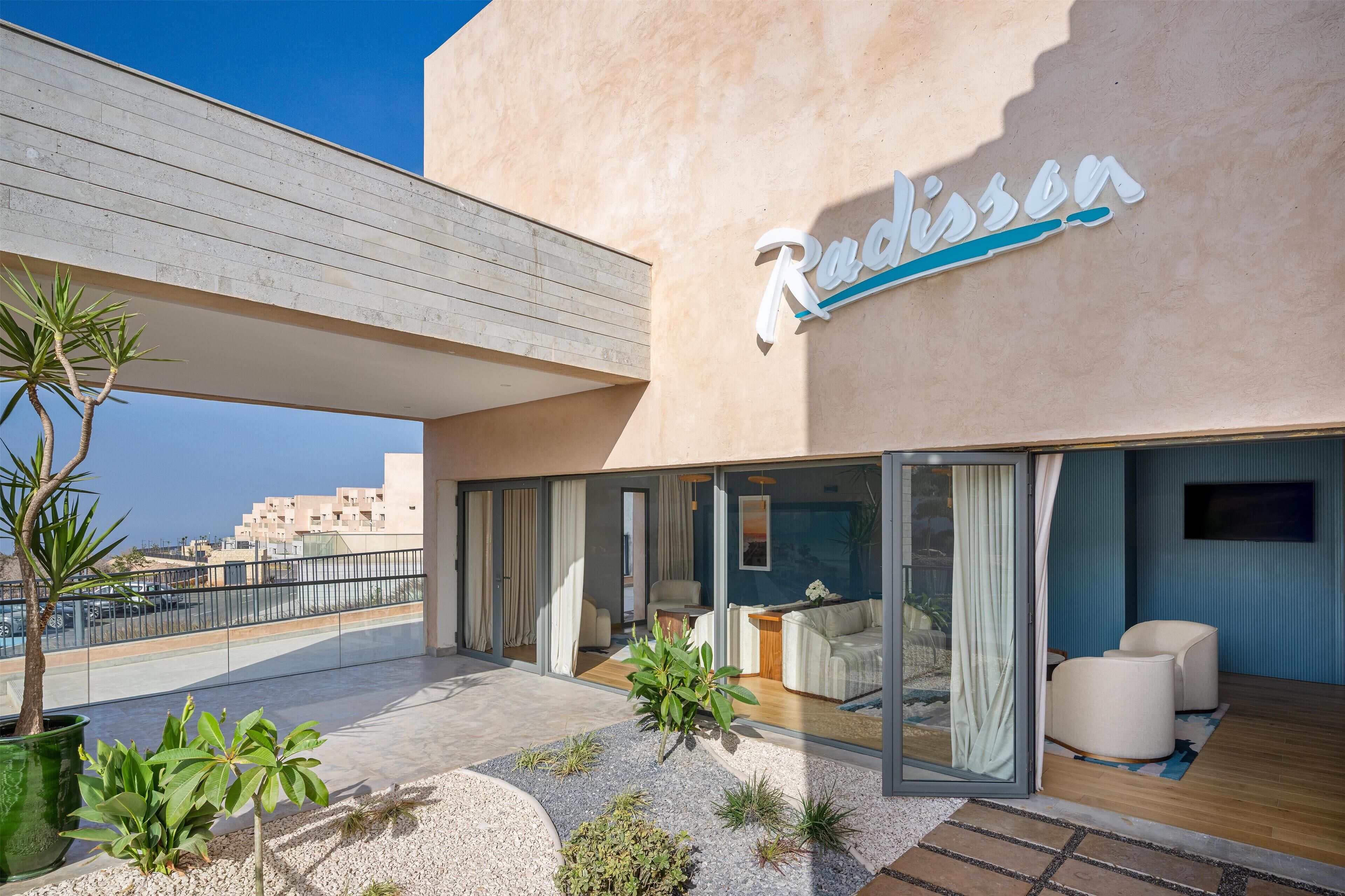 A modern building with a 'Radisson' sign, featuring a spacious balcony with seating, a pool area, and a view of the cityscape.