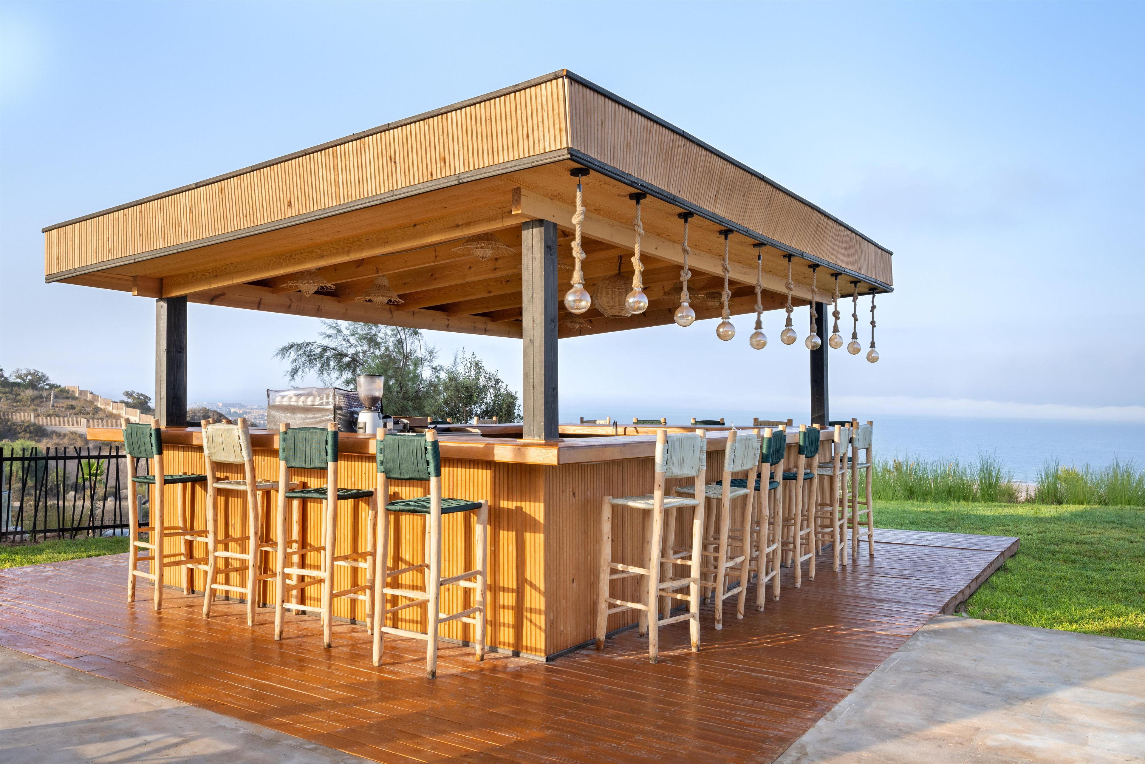 A wooden bar area with a covered seating arrangement and hanging light fixtures.