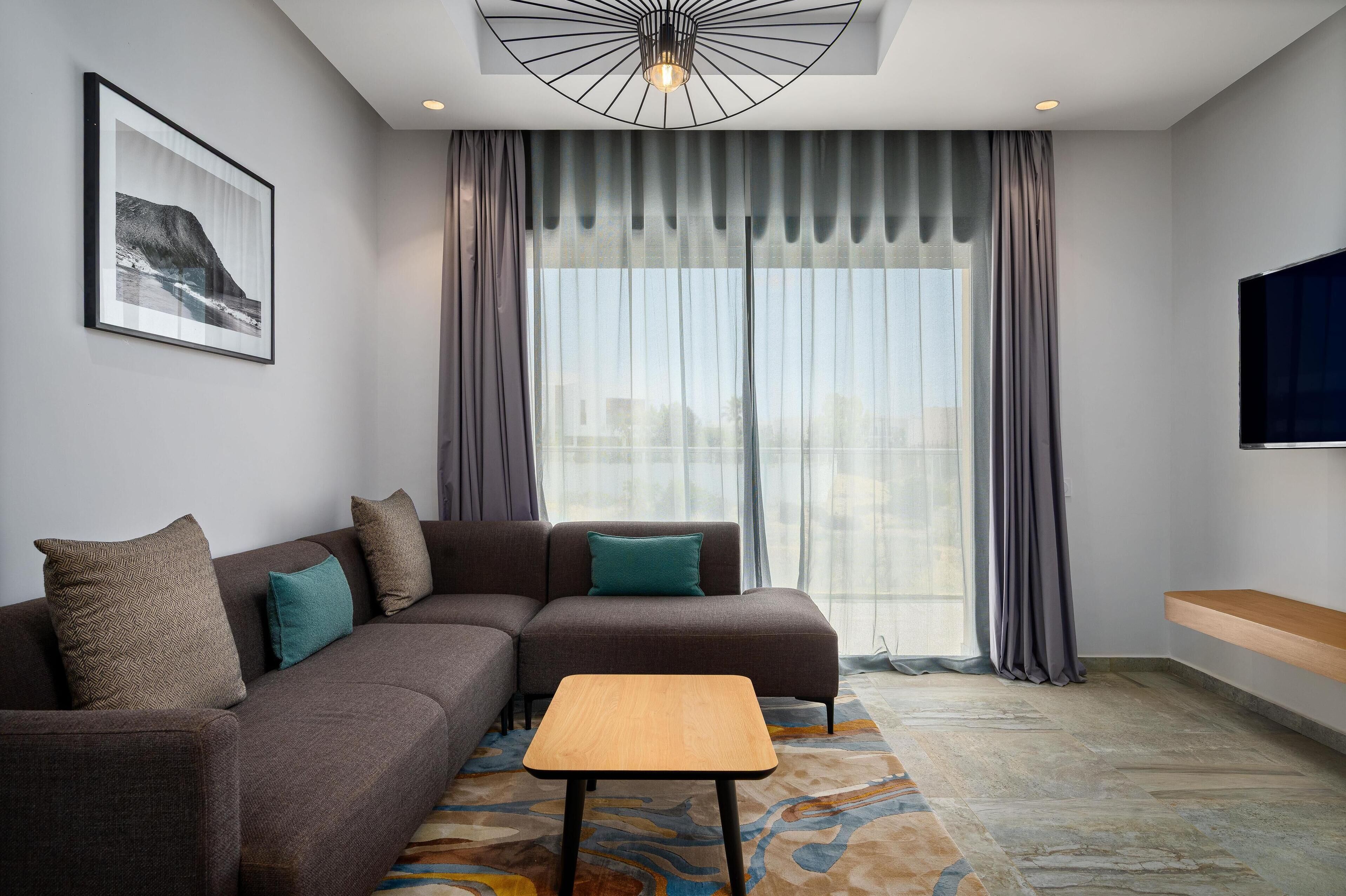 A modern living room with a sectional sofa, a wooden coffee table, and a large window with curtains.