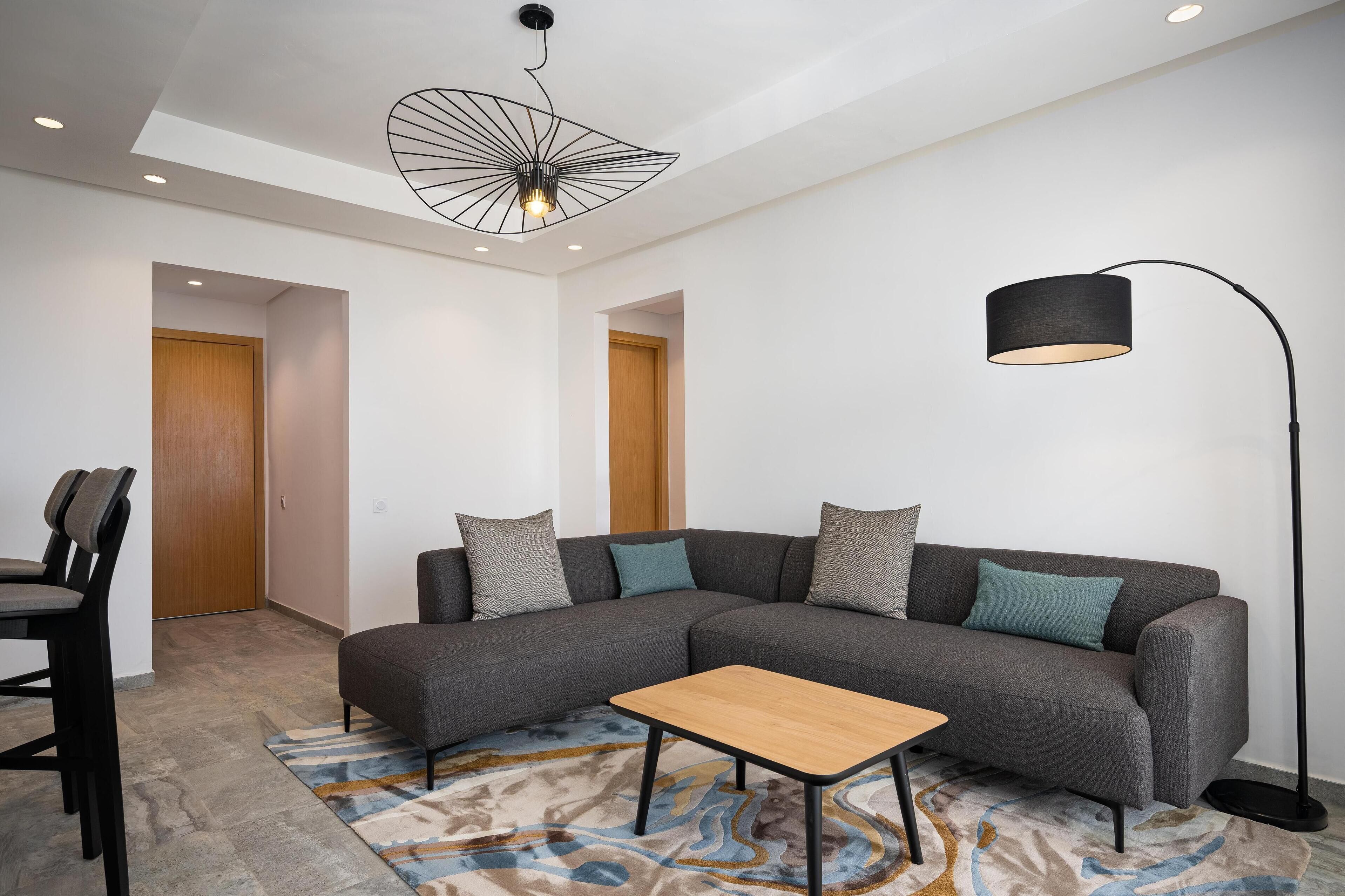 Un salon moderne avec un canapé d’angle, une petite table basse en bois, un lampadaire et un tapis à motifs.