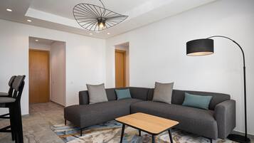 Un salon moderne avec un canapé d’angle, une petite table basse en bois, un lampadaire et un tapis à motifs.