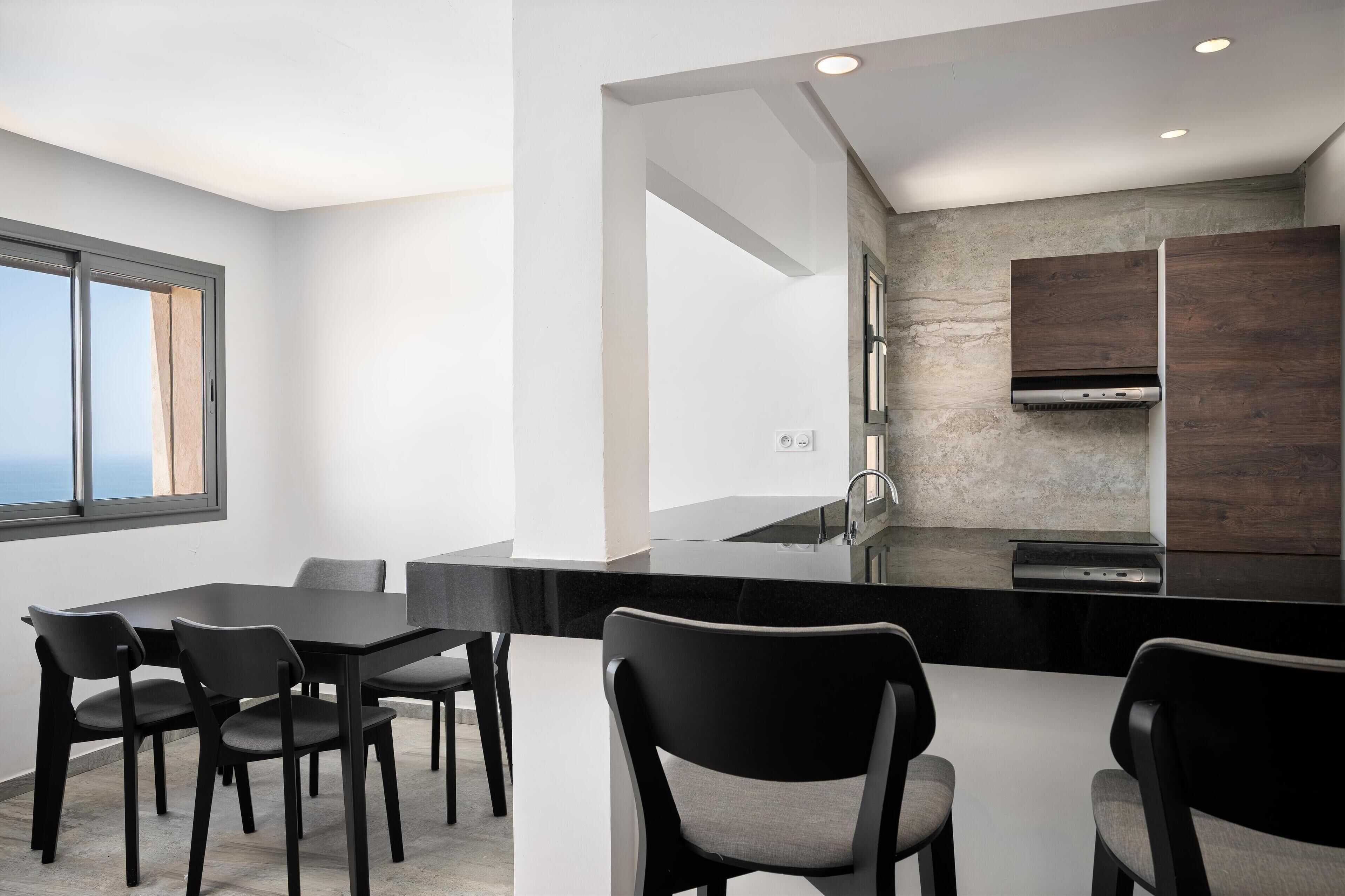 A modern kitchen with a black countertop, stainless steel appliances, and a view of the ocean.
