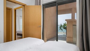 A hotel room with a bed, a wooden door, and a balcony with a view of the beach. - Radisson Residences Taghazout Bay (Taghazout)