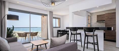 Una sala de estar moderna con sofá, sillas, una mesa y vista al océano a través de amplios ventanales.