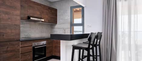 A modern kitchen with wooden cabinets, a built-in oven, and a bar area with two chairs.