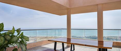 Un vaste balcon doté d’une table en bois et de bancs, offrant une vue sur une plage et la mer.