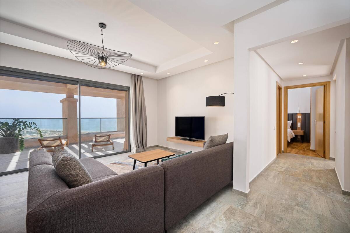 A modern living room with a sofa, TV, and a balcony with a view.