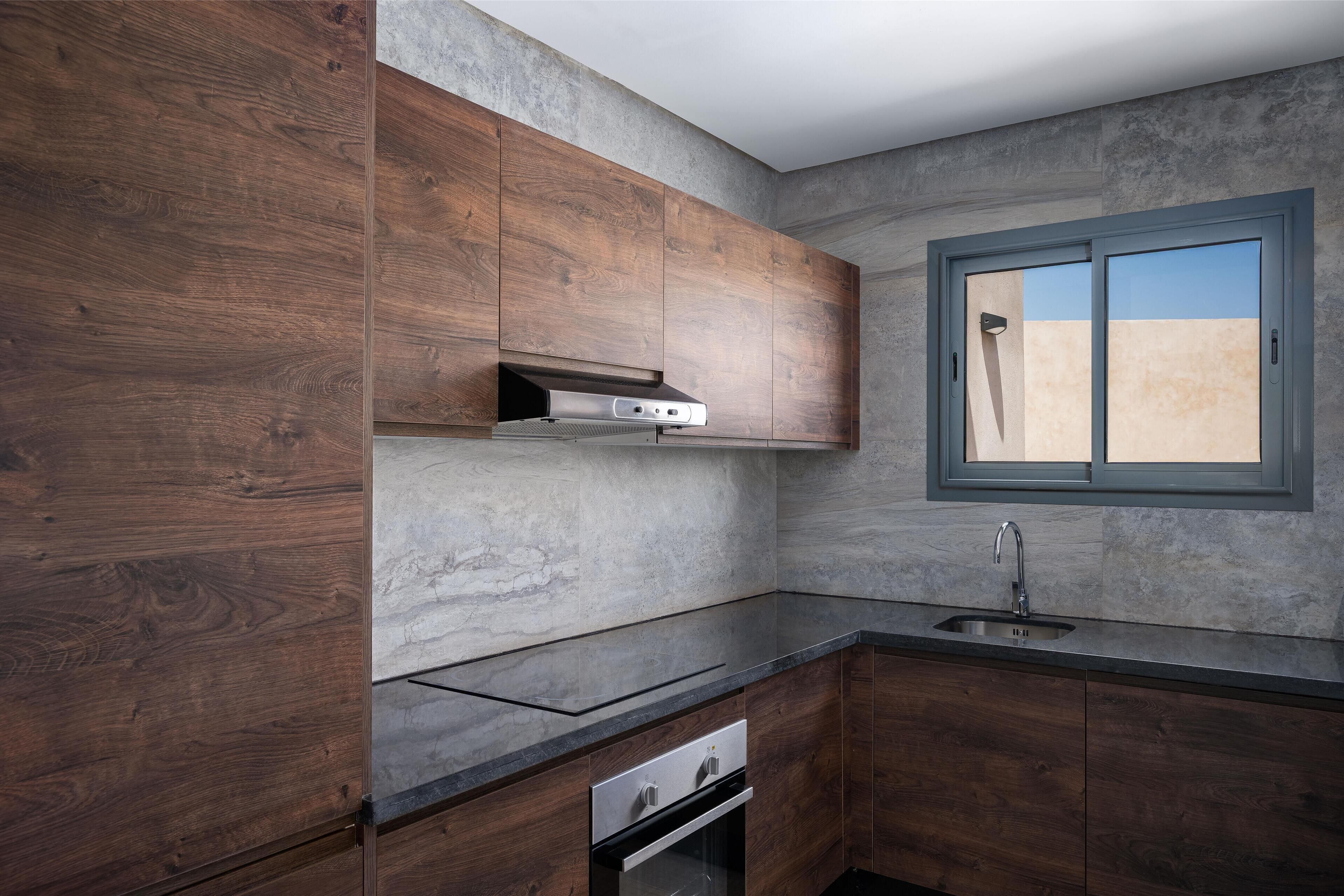 A modern kitchen with wooden cabinets, a built-in oven, a stainless steel sink, and a window with a view.