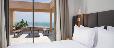 A hotel room with a large bed, a view of the ocean, and a balcony with outdoor furniture.