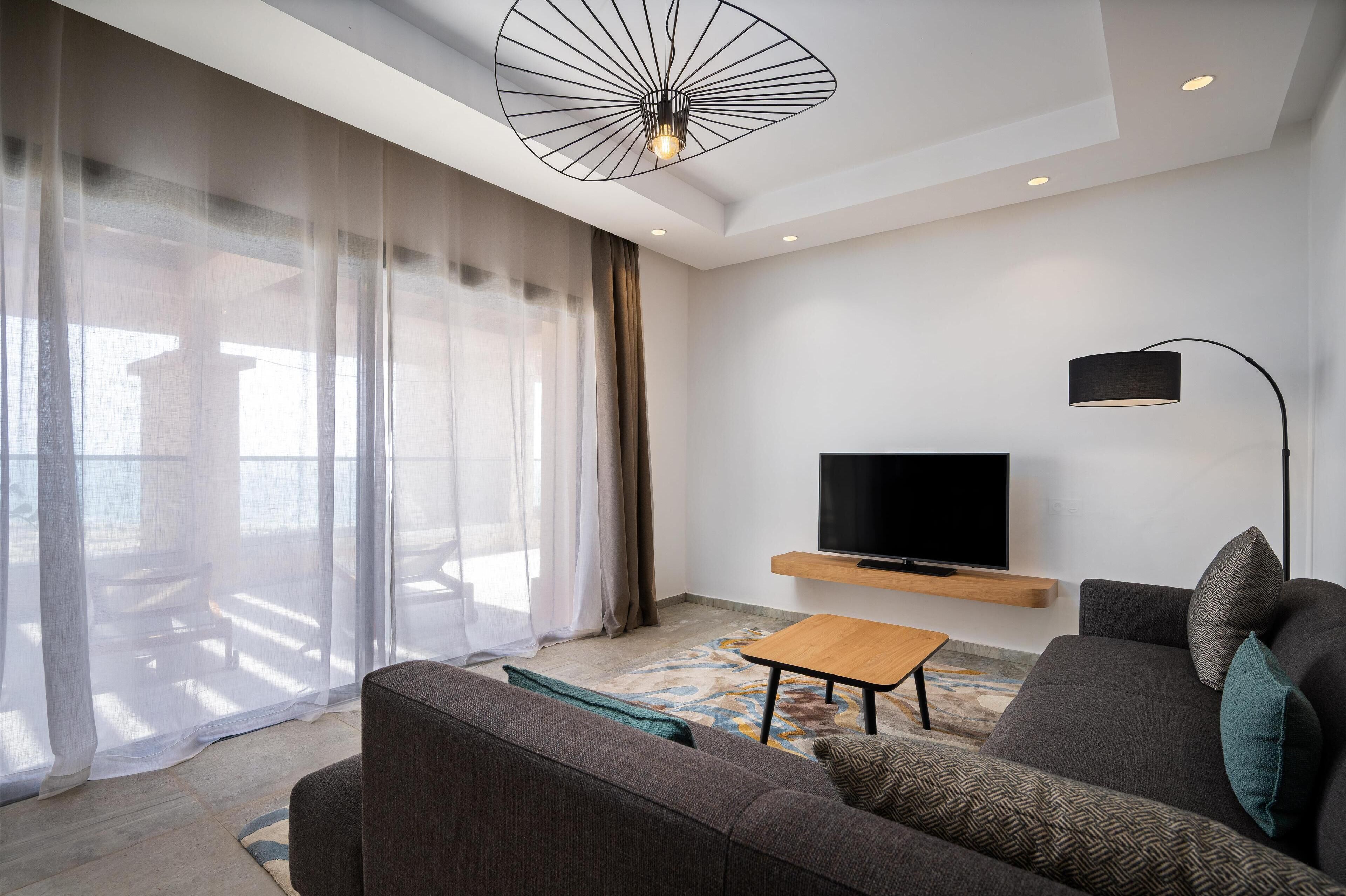 Un salon moderne avec un canapé, une table basse, un téléviseur fixé au mur et un luminaire suspendu au plafond.