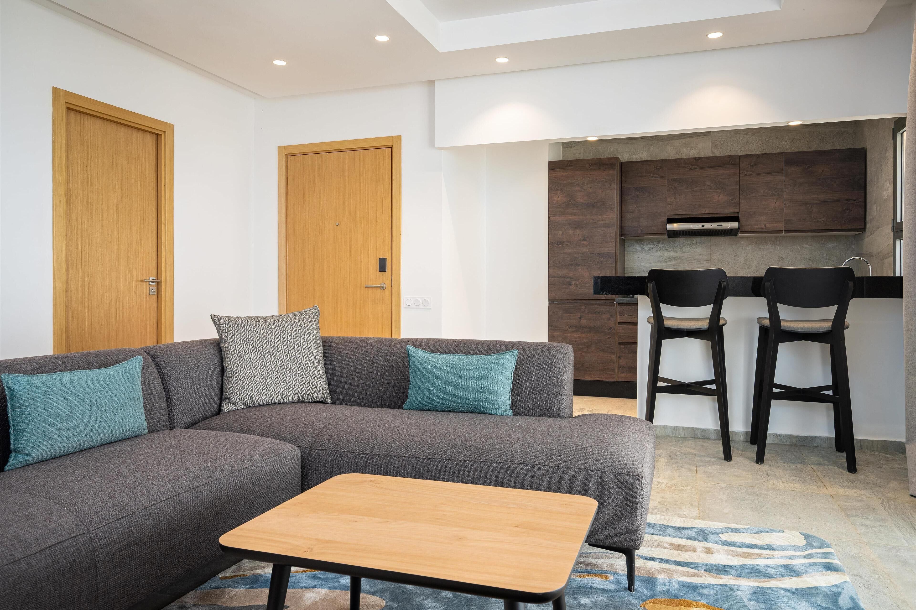 A modern living room with a grey sectional sofa, a wooden coffee table, and two black bar stools.