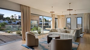 A modern living room with a sofa, armchairs, and a coffee table, large windows with curtains, and a view of the city. - Radisson Residences Taghazout Bay (Taghazout)