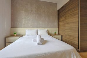 Habitación de hotel con una cama grande, dos mesitas de noche con lámparas, un cabecero de madera y un espejo amplio.