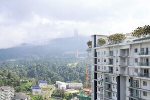 A multi-story residential building with balconies, a view of a forested area, and a distant city skyline. - Windmill Upon Hills Premier Suites by QHome (Genting Highlands)