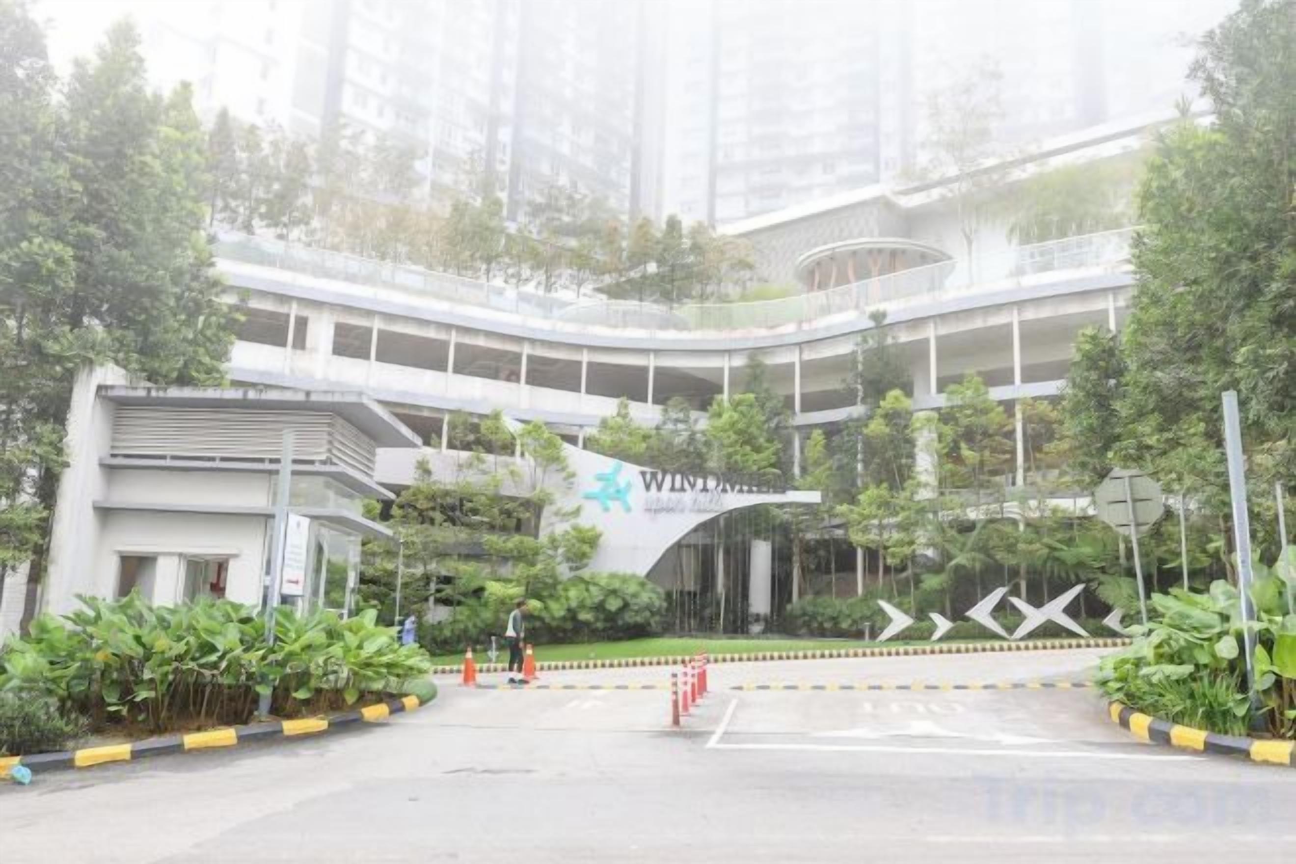 A multi-level building with a curved entrance, surrounded by greenery and a parking area.