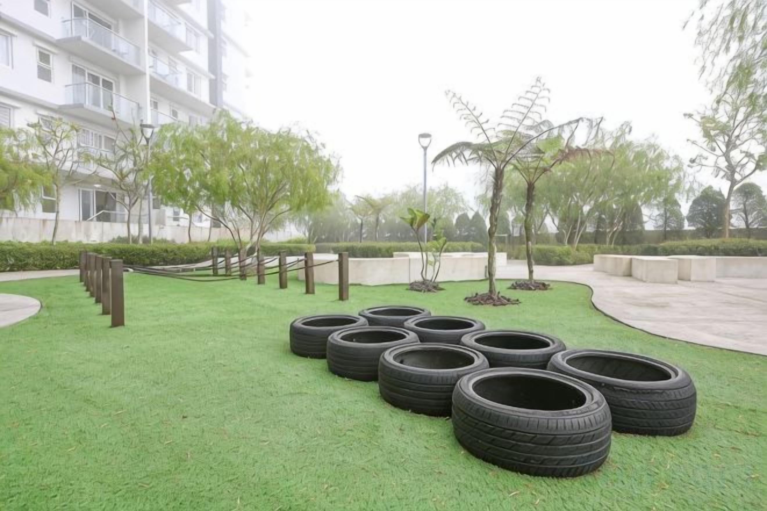 A grassy area with tires arranged in a circle, surrounded by trees and a building in the background.